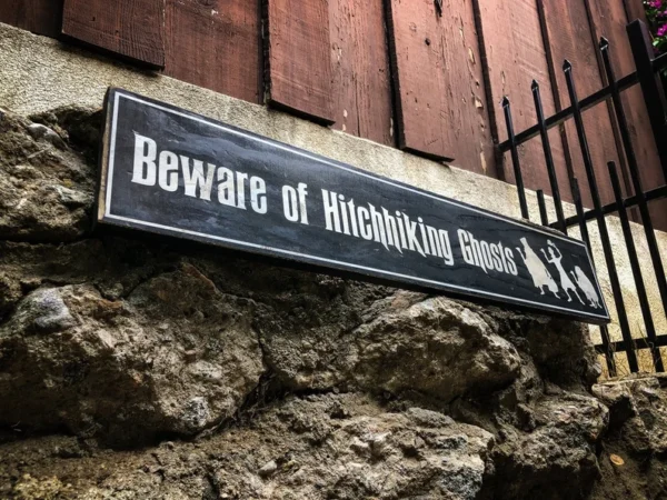 A sign on the side of a building that says beware of hitchhiking ghosts.