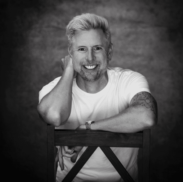 A man with blonde hair sitting in front of a wall.