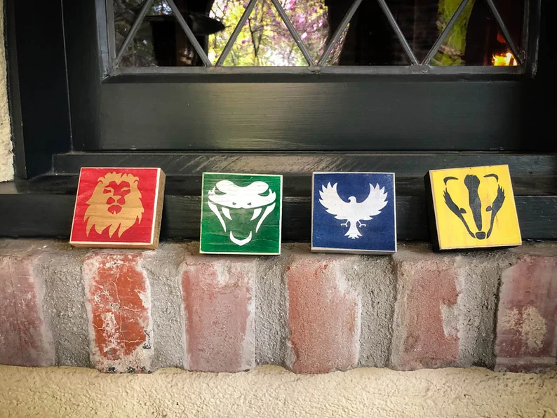 Here's an alt tag for the image: Four Hogwarts house crests on wood blocks.