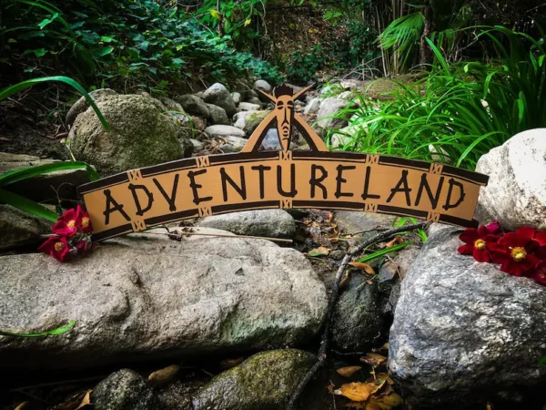 Adventureland sign by rocks and flowers.